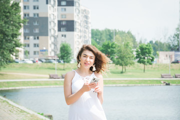 beautiful girl with a mobile phone walks through a city park on a hot summer day
