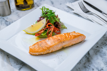 Salmon steak on the grill on white plate with lemon