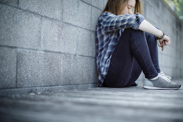 Young woman sits against grey cinder block wall