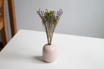 dry lilac and green flowers in pink small vase on white table and light background