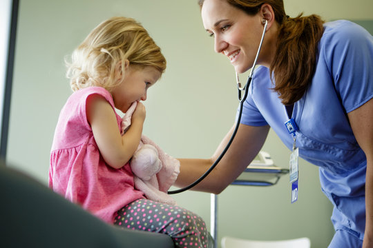 Woman doctor listens to stethoscope on young patient