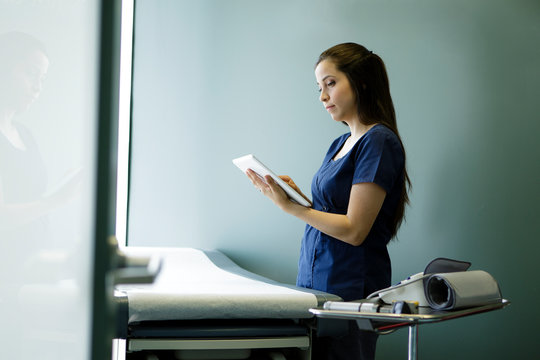 Nurse looking at tablet in empty examination room