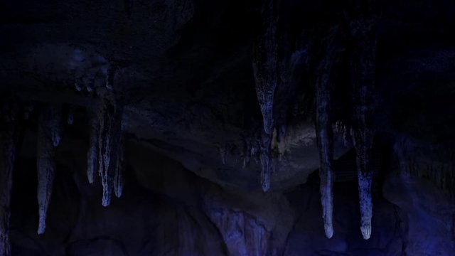 Stalactites in a cave above the underground lake. The slopes of the cave are illuminated with blue light.