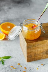 Homemade orange jam in glass jar on the wooden box on the gray background. Orange jam in swing-top jar on wood with orange slices in the back. Food photography. Seasonal cooking