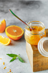Homemade orange jam in glass jar on the wooden box on the gray background. Orange jam in swing-top jar on wood with orange slices in the back. Food photography. Seasonal cooking