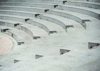 Rows of grayish stony or marble seats and flights of stairs of a modern outdoor amphitheater with a...