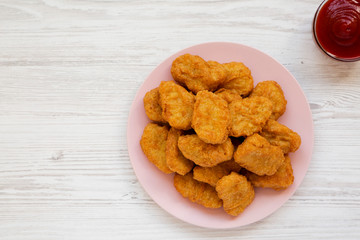 Chicken nuggets on a pink plate, ketchup on a white wooden surface, top view. Overhead, from above, flat lay. Copy space.