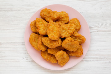 Overhead view, chicken nuggets on a pink plate on a white wooden background, top view. Overhead, from above, flat lay. Close-up.