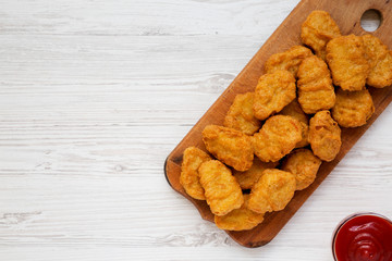 Overhead view, chicken nuggets on a rustic wooden board on a white wooden background. Flat lay, from above, top view. Copy space.
