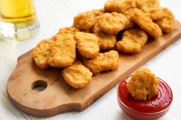 Chicken nuggets with ketchup and glass of cold beer on a white wooden background, low angle view. Closeup.