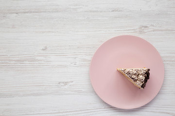 A piece of tiramisu cake on a pink plate on a white wooden background, top view. Copy space.