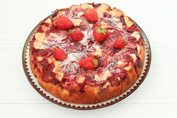 Pie with strawberries located on a plate on a white background, top view