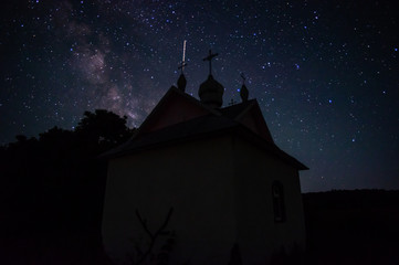 Little chapel in the forest against the background of the night starry sky