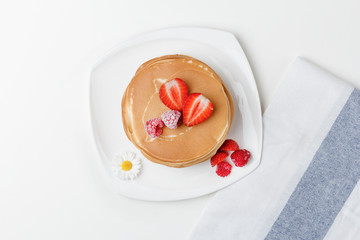 Homemade breakfast. American style pancakes served with fresh strawberry and .frozen raspberry on white table and towel. Top view