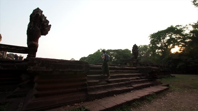 Woman tourist with backpack is going upstairs between two seven-headed naga statues in early morning at Angkor Wat temple. Cambodia