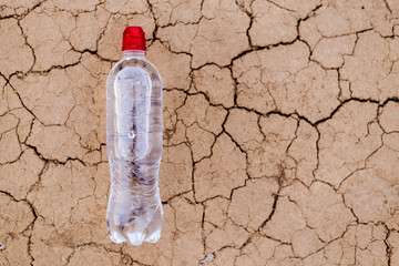 A bottle of water on the dried, cracked soil.