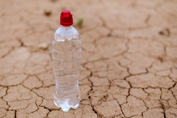 A bottle of water on the dried ground. The concept of thirst, dehydration.