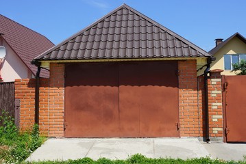 facade of a brown garage with metal gates under a tiled roof in the street