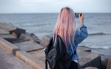 young girl with pink hair with black backpack admiring the sea