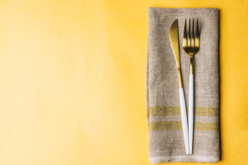 Fork, knife and linen napkin on yellow background