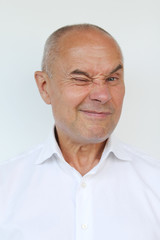 bald old man in a white shirt showing grimaces, winks, close-up