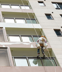 worker hanging with ropes and painting the oustside of a highrise building