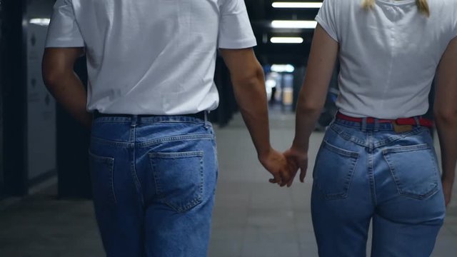 Slow motion, young unrecognizable couple walking along the sidewalk, hugging the waist and holding hands. Happy couple in stylish clothes. View from behind