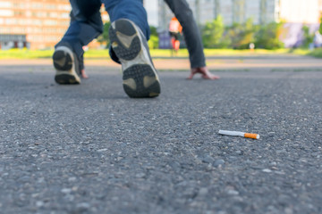 an abandoned Smoking cigarette butt lies on the asphalt path against the background of a man's legs who is preparing to run sprint