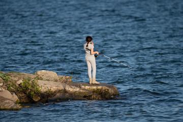 unknown girl is fishing from the point while swatting at the mosquitoes