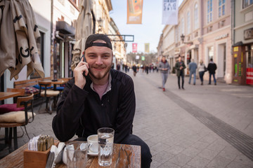 one young man, talking over phone, sitting in cafe on a street.