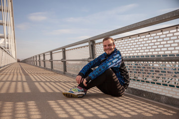 one young man - jogger on a bridge, sitting on a asphalt.