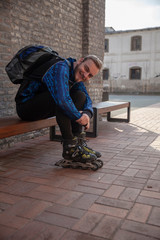 one young man, wearing inline skates, sitting on a bench. Smiling and happy.