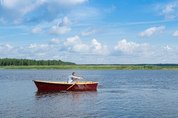 man paddles in a wooden boat, swims on the lake on a sunny day, active weekend