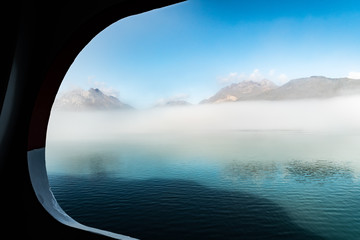 Obscured foggy view of Alaska Glacier Bay mountain range through cruise ship window port hole sailing through the inlet basin in October, autumn/fall season. Scenic nature landscape and wildlife tour.