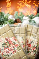 Handmade chocolates bar. Christmas theme. White chocolate bar with pistachio nuts and dried fruit cherries. Garland lamps bokeh on background. Copy space