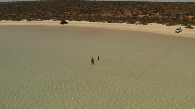 drone view of shallows of isolated beach with two people and a distant car coming into view