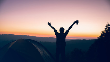 freedom time of hiker man holding coffee cup near camping tent on mountains at sunset background. travel concept.