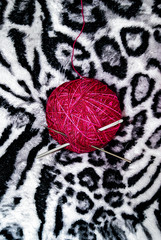 pink wool yarn ball with two crochet needles in soft black and white zebra blanket
