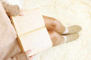 Woman is reading book on white shaggy blanket reading book