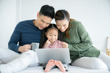 Parents having fun with their little daughter on bed with tablet. Family spending time at the holiday , happy family concept.