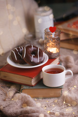Still life details in home interior of living room. Cup of tea and chocolate donuts on stack of book. Tea leisure time in autumn and winter. Cozy relax seasonal concept.