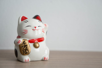 Maneki neko lucky cat show text on hand meaning rich on wood table background, select focus