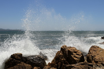 Big storm waves hitting the coastal rocks of the sea. Sunny windy day, blue sky. Splashes and foam....
