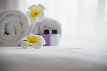 Obraz na płótnie Canvas Hotel towel and shampoo and soap bath bottle set on white bed with plumeria flower decorated - relax vacation at the hotel resort concept
