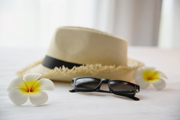 Tourist stuff hat sun glasses and plumeria flower in white bed room - happy relax vacation holiday and hotel concept