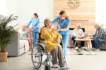 Verpleegkundige glas water geven aan oudere vrouw in rolstoel bij bejaardentehuis. Senioren helpen