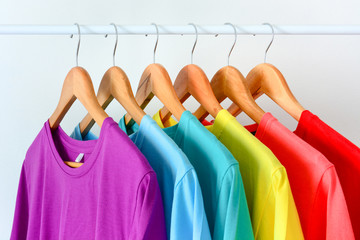 close up collection of colorful rainbow t-shirts hanging on wooden clothes hanger in closet or...