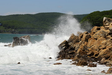 Big storm waves hitting the coastal rocks of the sea. Sunny windy day, blue sky. Splashes and foam. Storm landscape.