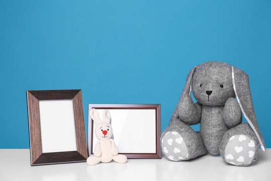 Photo frames and adorable toy bunnies on table against color background, space for text. Child room elements