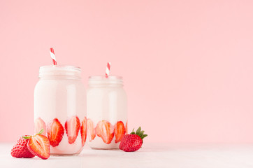 Strawberry smoothies in retro glass jars with bright sliced berries, straws on light, soft, pink background, copy space.